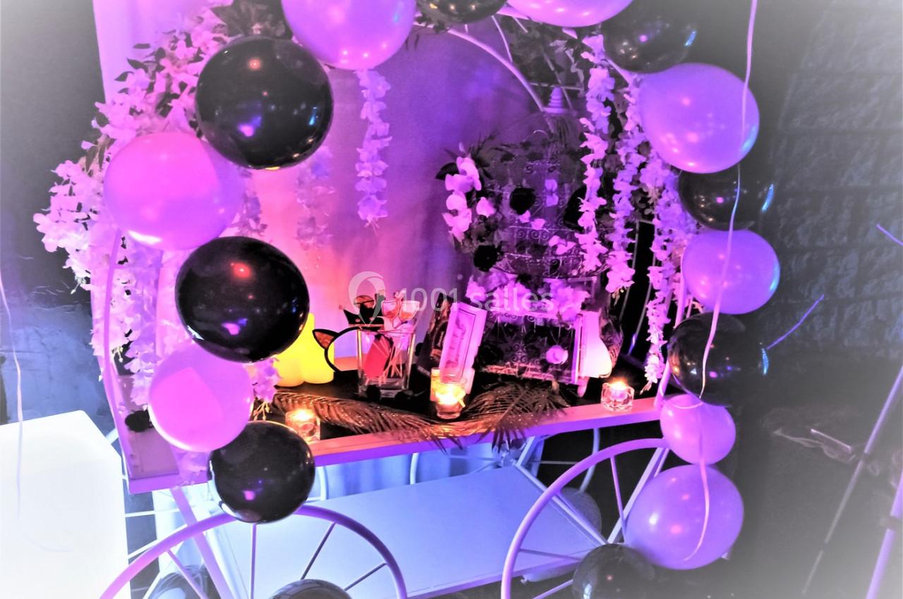 Décoration festive avec ballons noirs et violets, guirlandes florales et bougies sur une table illuminée.