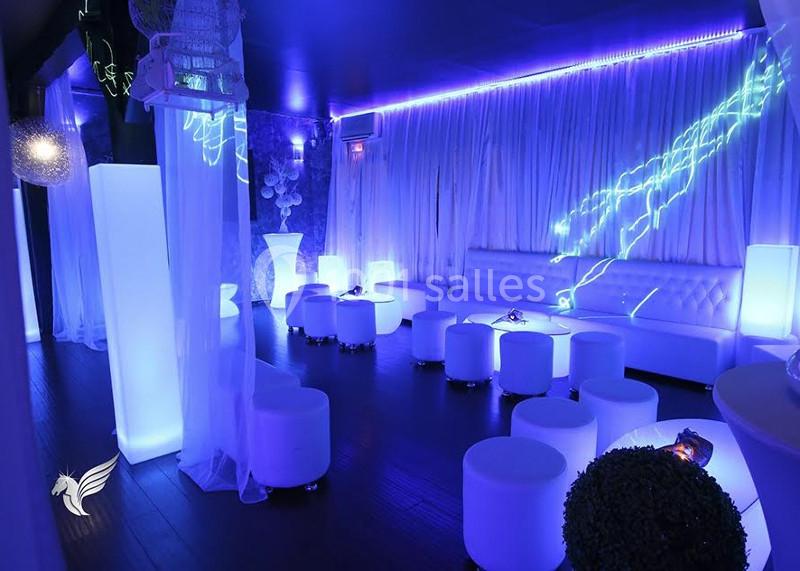 Salle moderne avec éclairage LED bleu, mobilier blanc minimaliste et rideaux lumineux en arrière-plan.