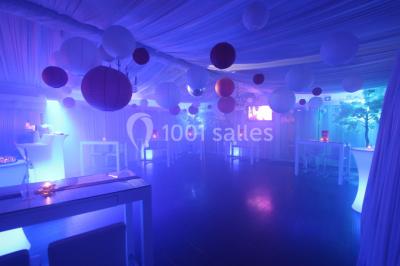 Salle de réception décorée en noir et blanc avec tables dressées, chaises blanches et lanternes suspendues.