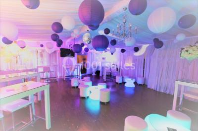 Salle de réception décorée en noir et blanc avec tables dressées, chaises blanches et lanternes suspendues.