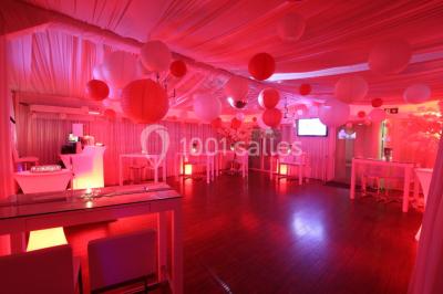 Salle de réception décorée en noir et blanc avec tables dressées, chaises blanches et lanternes suspendues.