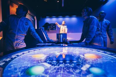Un groupe de personnes en tenue uniforme observe et interagit avec un écran dans un environnement futuriste.