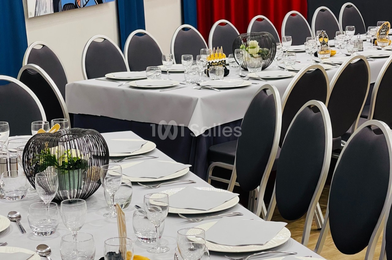 Tables dressées avec nappes blanches, assiettes, verres et décorations modernes dans une salle aux rideaux colorés.
