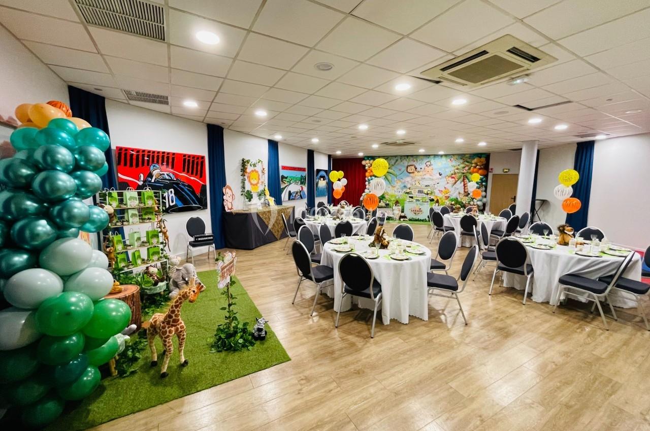 Salle décorée pour une fête avec ballons, tables dressées et thème jungle, incluant des figurines d'animaux.