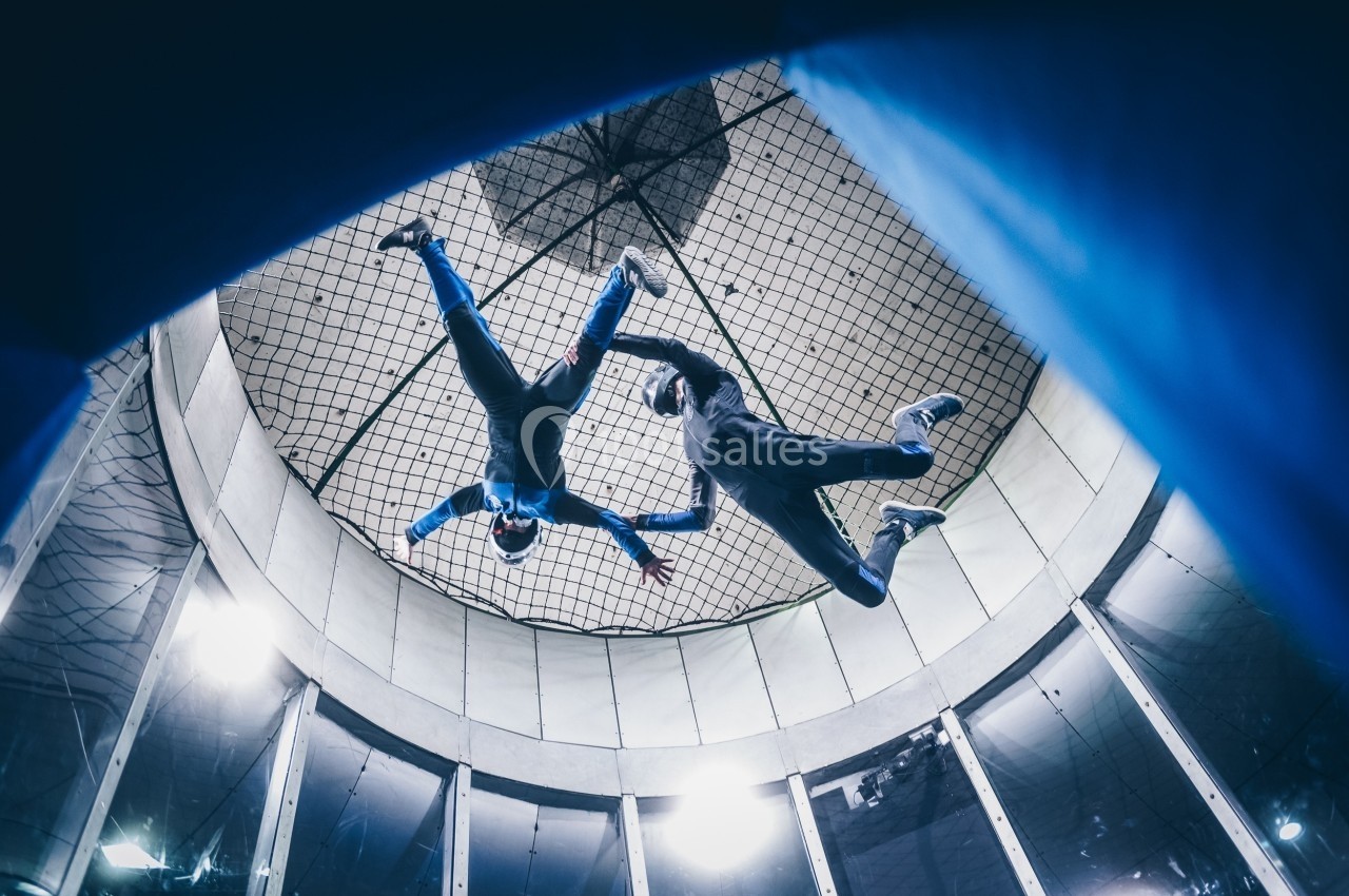 Deux personnes en combinaison effectuent une chute libre simulée dans un tunnel vertical sous un filet.