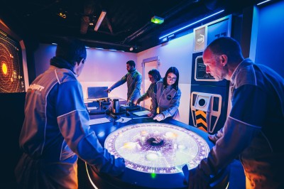 Un groupe de personnes en tenue uniforme observe et interagit avec un écran dans un environnement futuriste.