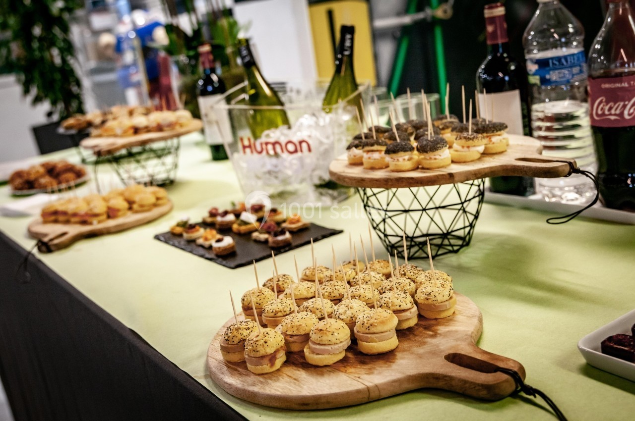 Plateau de mini-burgers et amuse-bouches variés disposés sur une table avec des bouteilles de vin en arrière-plan.