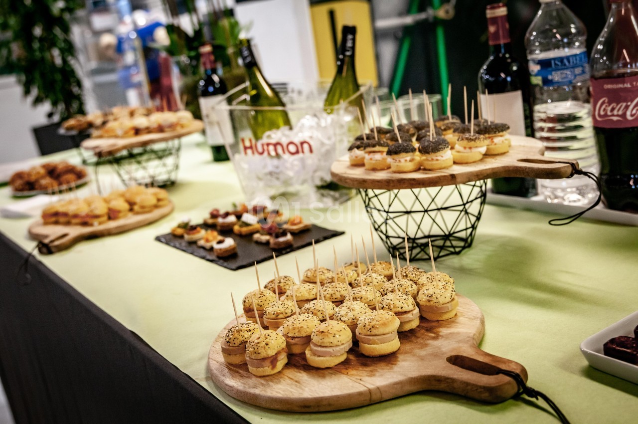 Plateau de mini-burgers et amuse-bouches variés disposés sur une table avec des bouteilles de vin en arrière-plan.