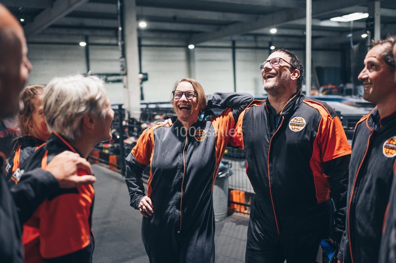 Un groupe de personnes en tenue de karting sourit et discute dans un espace intérieur.