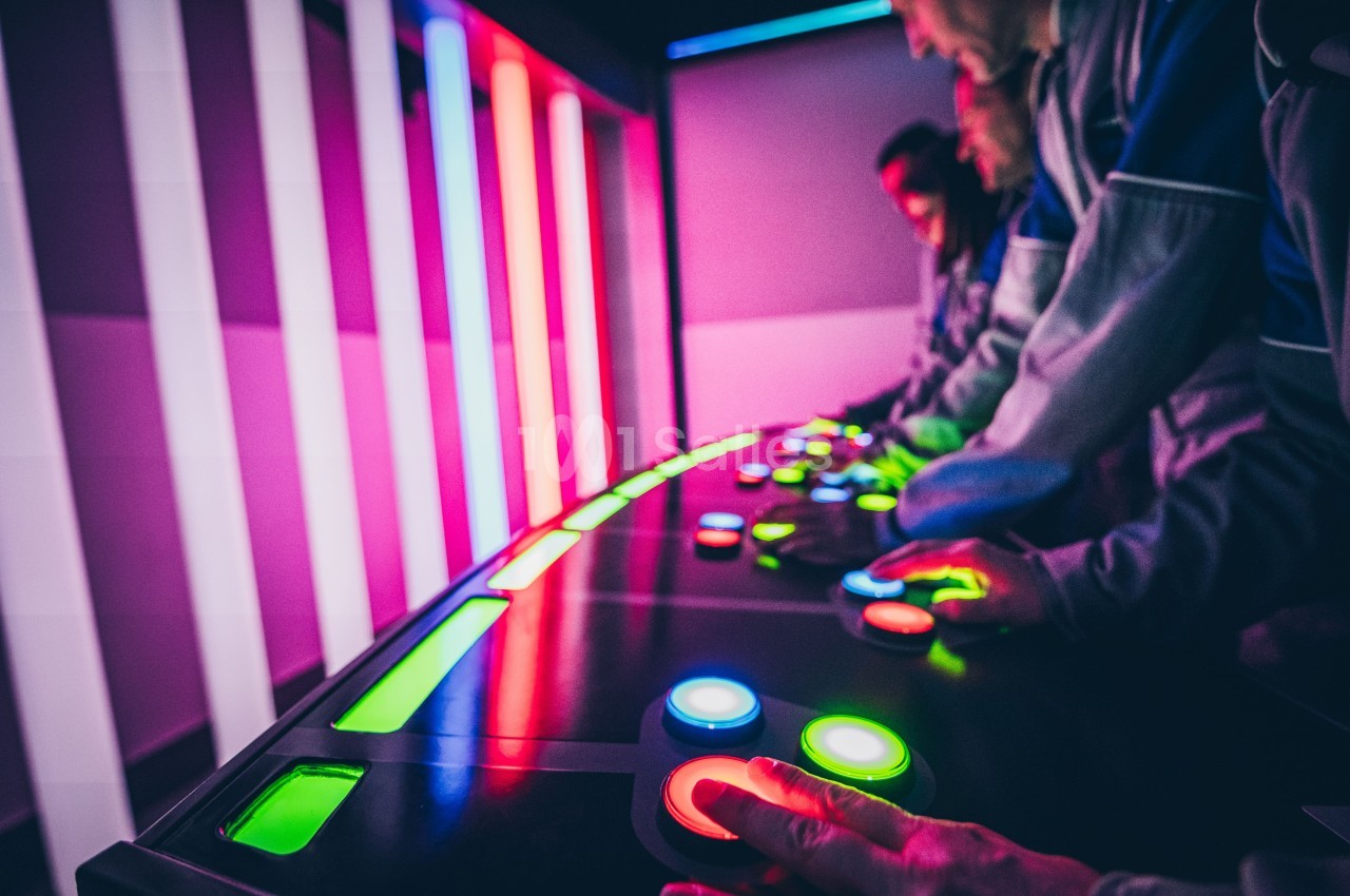 Des personnes interagissent avec un tableau de contrôle lumineux doté de boutons colorés dans un environnement sombre.