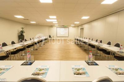 Salle de conférence vide avec des rangées de chaises noires et un écran affichant le logo ’Aerokart’.