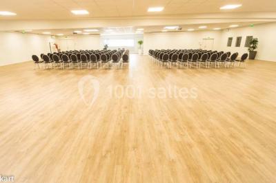 Salle de conférence vide avec des rangées de chaises noires et un écran affichant le logo ’Aerokart’.