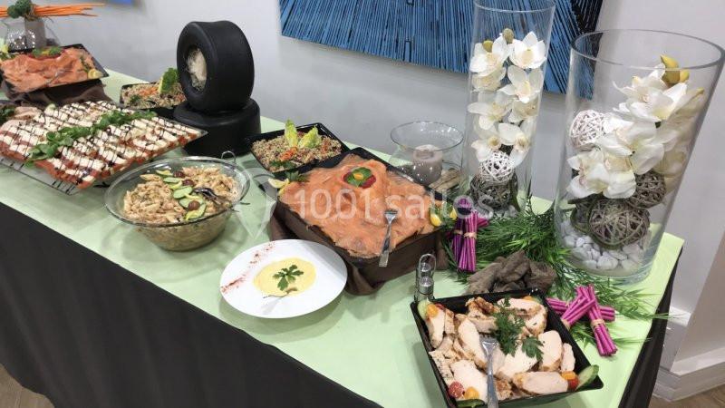 Buffet varié avec saumon fumé, salade, charcuterie, légumes et décorations florales sur une nappe verte.