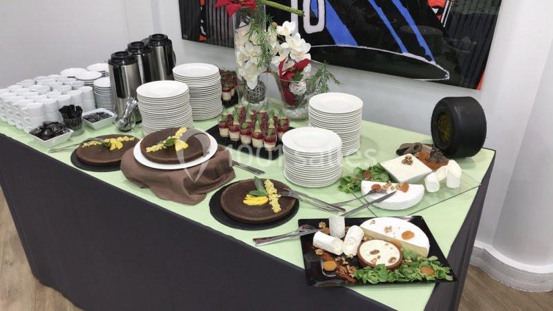 Buffet avec gâteaux au chocolat, fromages, verrines, assiettes empilées et carafes sur une nappe verte.