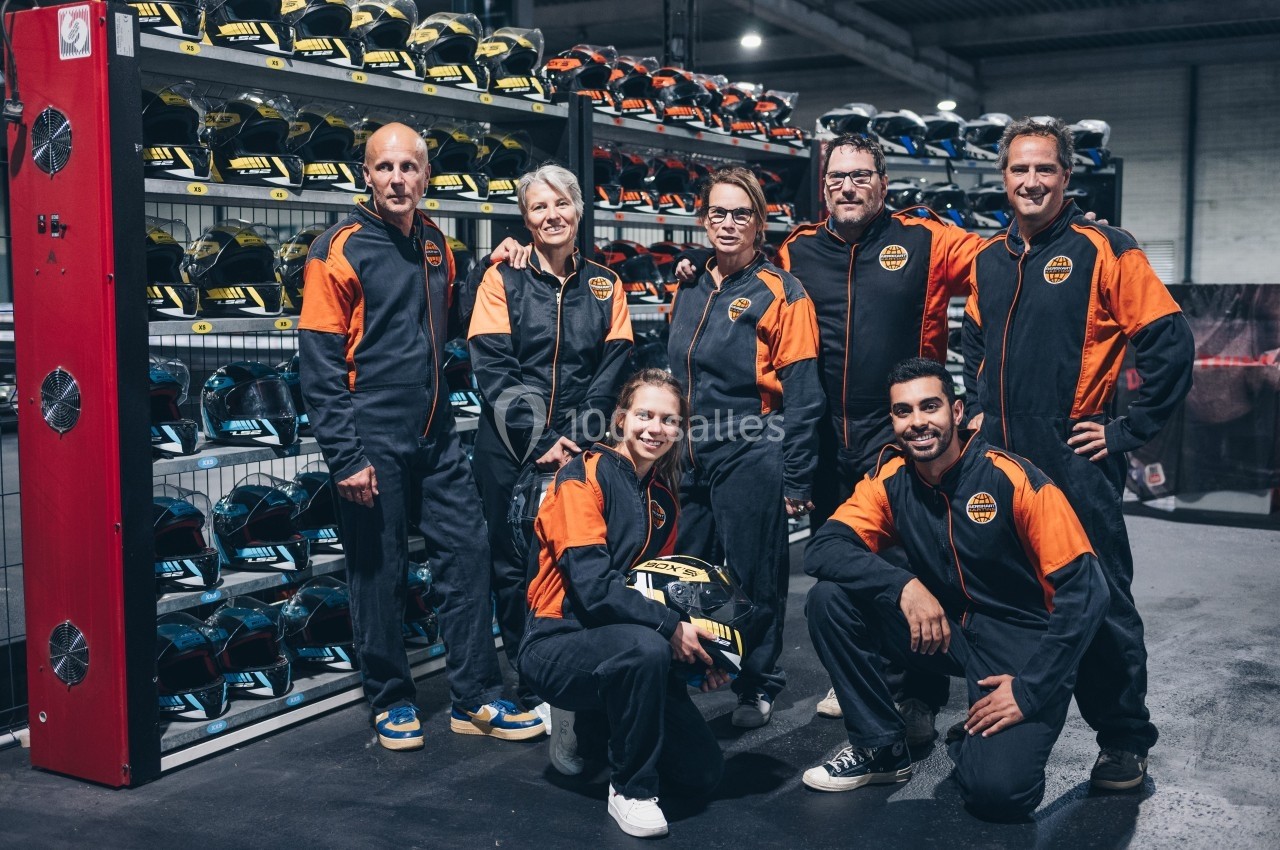 Un groupe de personnes en tenue de karting posant devant des étagères remplies de casques colorés.