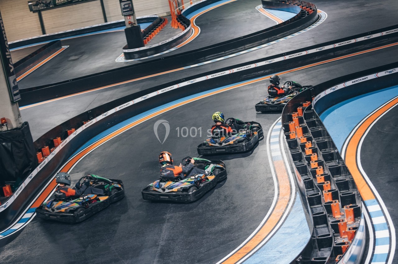 Quatre personnes conduisent des karts sur une piste intérieure avec des virages marqués et des bordures colorées.