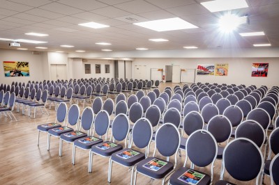 Salle de conférence vide avec des rangées de chaises noires et un écran affichant le logo ’Aerokart’.