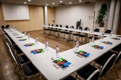 Salle de conférence vide avec des rangées de chaises noires et un écran affichant le logo ’Aerokart’.