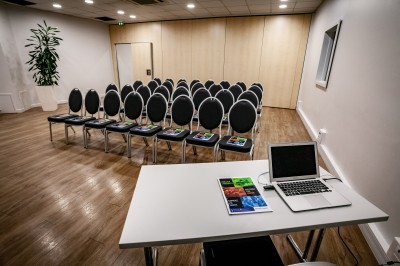 Salle de conférence vide avec des rangées de chaises noires et un écran affichant le logo ’Aerokart’.