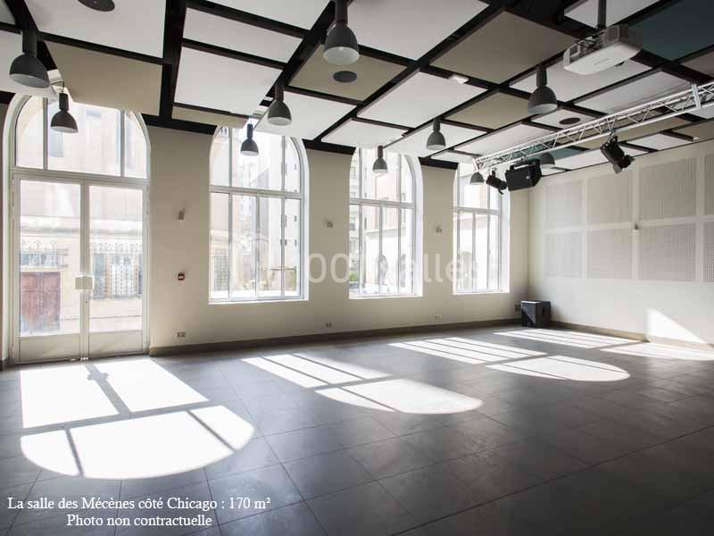 Salle lumineuse avec de grandes fenêtres cintrées, sol en carrelage gris et plafond équipé de panneaux acoustiques.