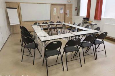 Disposition en U de tables blanches avec chaises noires dans une salle de réunion équipée d'un tableau et d'une fontaine à…