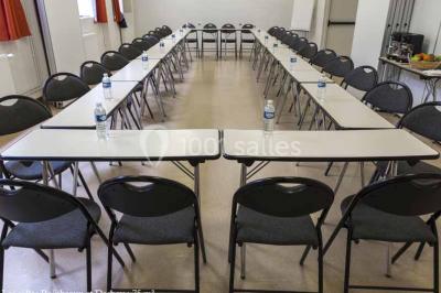 Disposition en U de tables blanches avec chaises noires dans une salle de réunion équipée d'un tableau et d'une fontaine à…