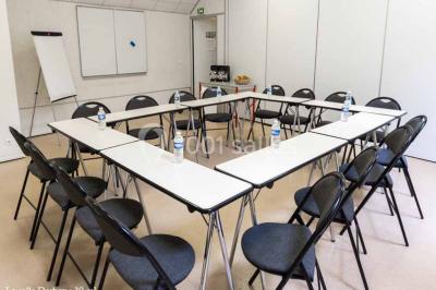 Disposition en U de tables blanches avec chaises noires dans une salle de réunion équipée d'un tableau et d'une fontaine à…