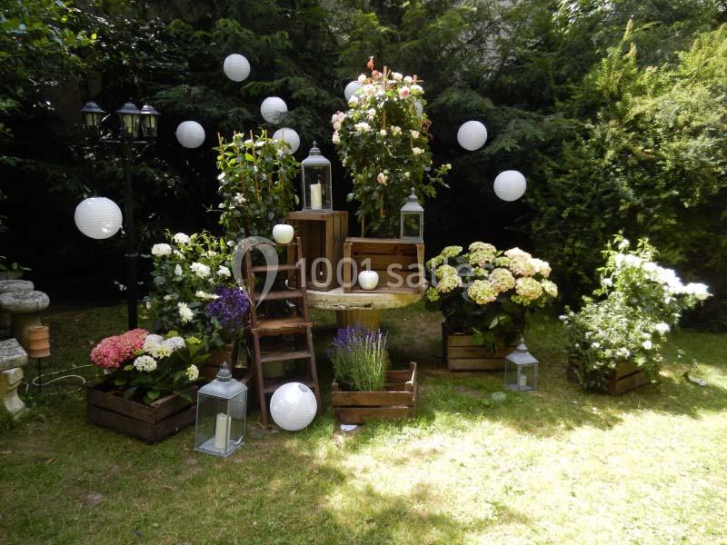 Décoration florale extérieure avec lanternes, caisses en bois, fleurs colorées et lampions blancs dans un jardin verdoyant.