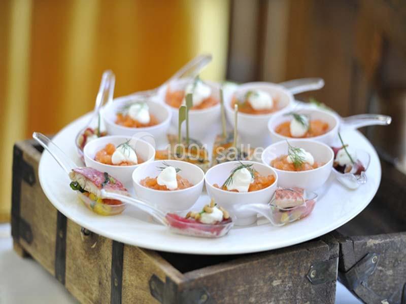 Plateau de verrines et cuillères apéritives garnies de saumon, crème et herbes fraîches, présenté sur un support en bois.