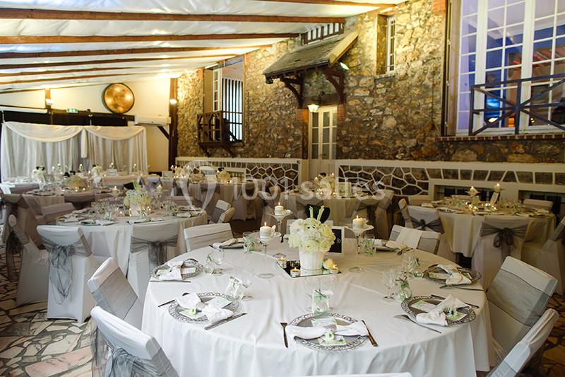 Salle de réception décorée pour un mariage, avec tables rondes dressées, nappes blanches et décorations élégantes.