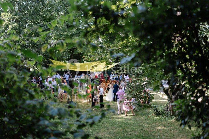 Groupe de personnes réunies dans un jardin verdoyant sous une grande toile jaune, entourées d'arbres.