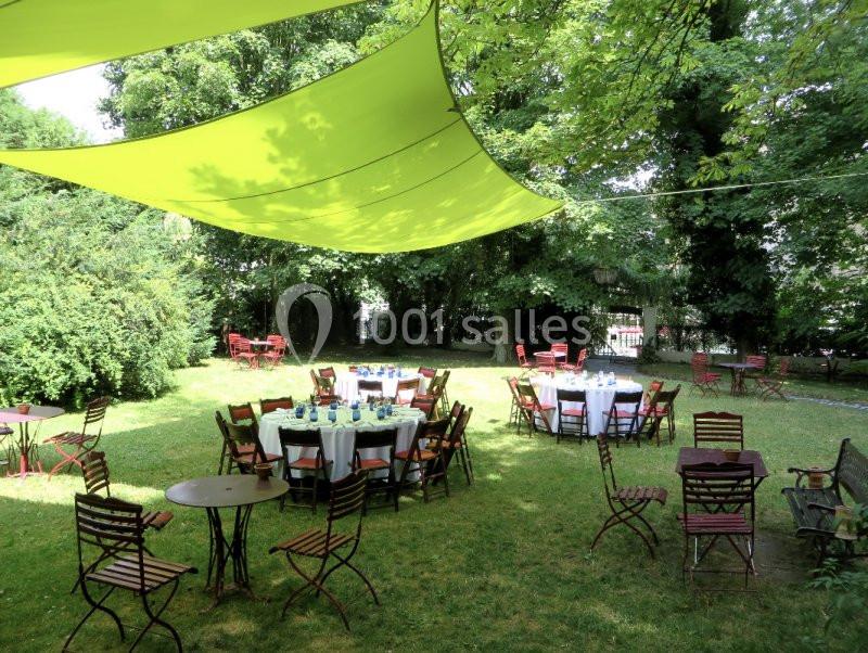 Jardin ombragé avec tables et chaises disposées pour un repas en plein air, entouré de verdure.