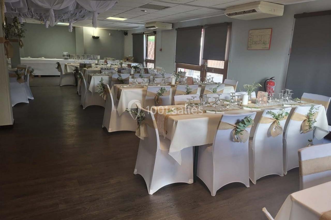 Salle de réception décorée avec des tables dressées, nappes blanches et éléments naturels pour un événement festif.