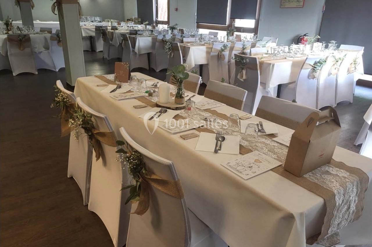 Salle de réception décorée pour un événement, avec tables dressées, nappes blanches et ornements en toile de jute.