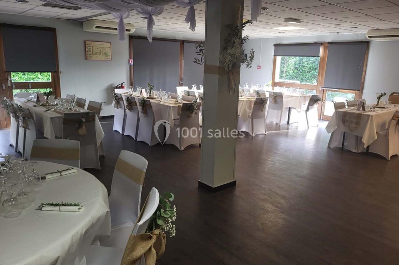 Salle de réception décorée avec des tables rondes et rectangulaires, nappes blanches et ornements naturels.