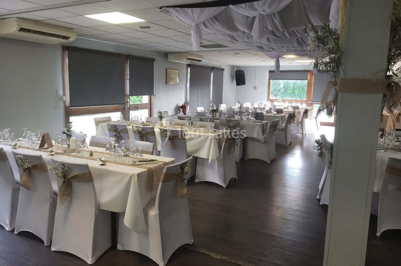 Salle de réception décorée avec des tables dressées, nappes blanches, chaises ornées et plafond drapé de tissu blanc.