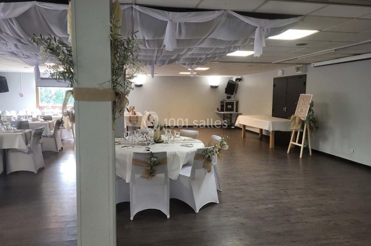 Salle de réception décorée avec des tables rondes dressées, nappes blanches et ornements floraux, plafond drapé.
