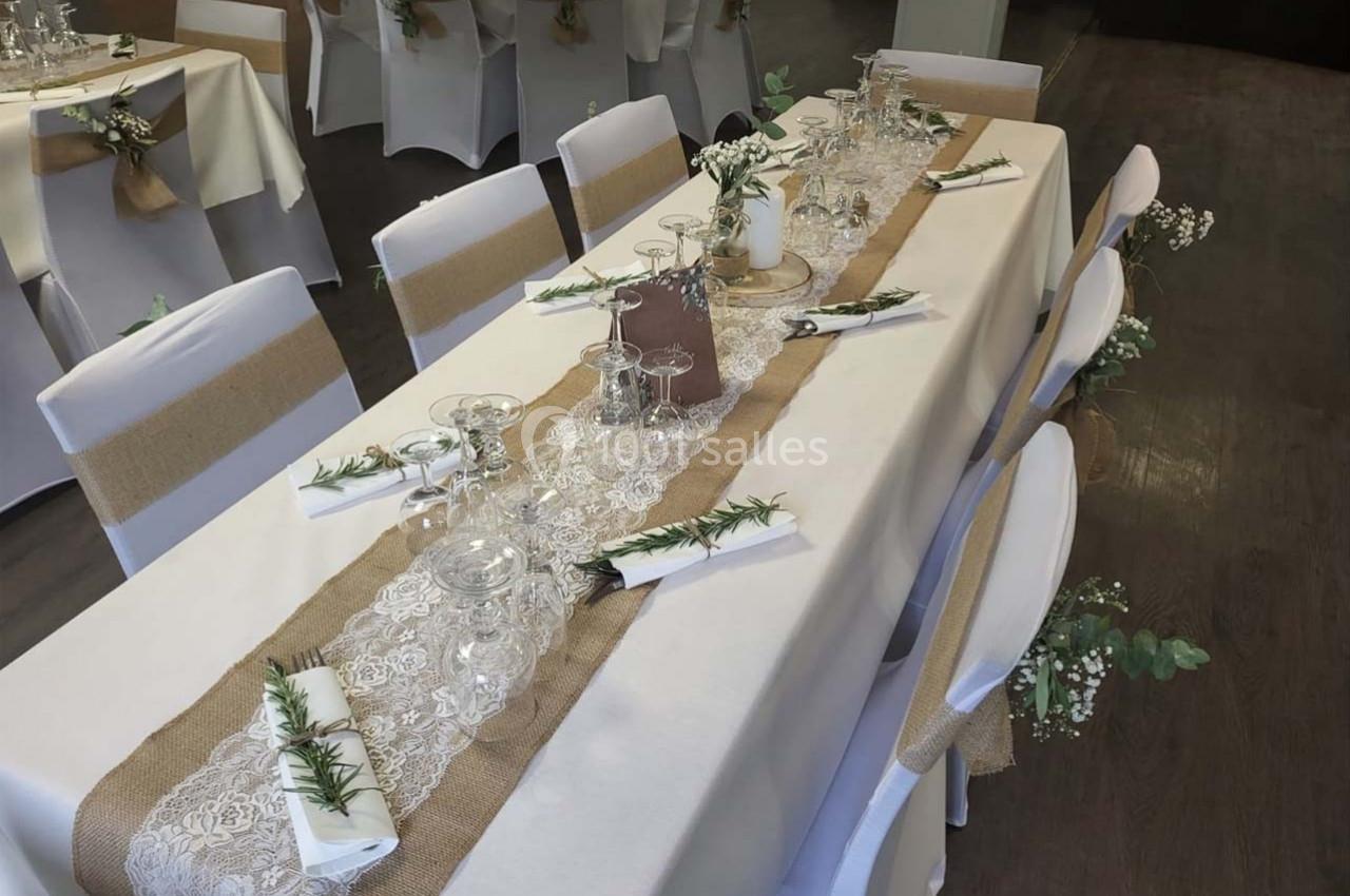 Table décorée pour un événement, avec nappes blanches, chemins de table en toile de jute, verres et décorations florales.