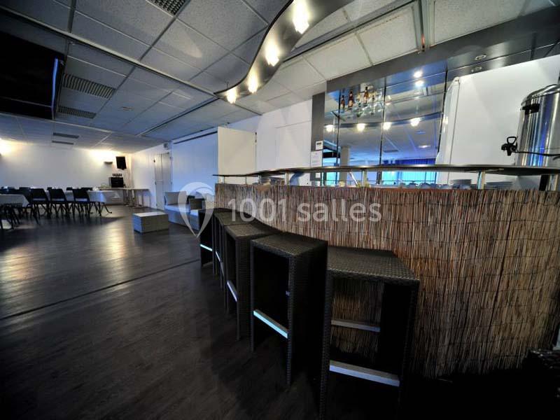 Bar avec comptoir en bambou, tabourets en osier et salle de réception avec tables et chaises en arrière-plan.