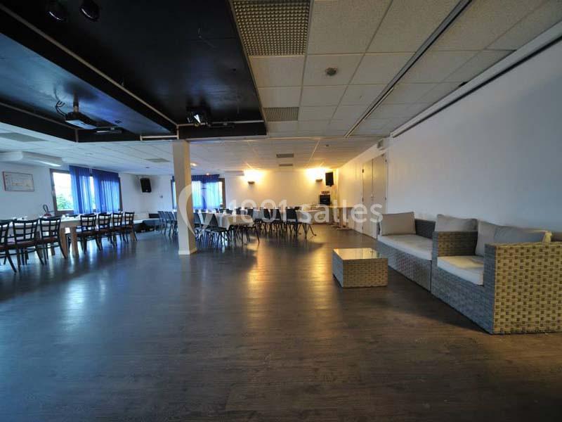 Salle spacieuse avec parquet, tables et chaises alignées, canapés en rotin sur le côté et grandes fenêtres avec rideaux…