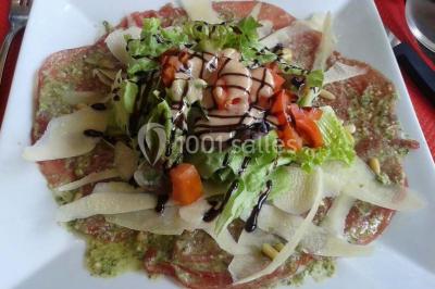 Assiette de carpaccio de bœuf garnie de salade, copeaux de parmesan, tomates et filet de sauce balsamique.
