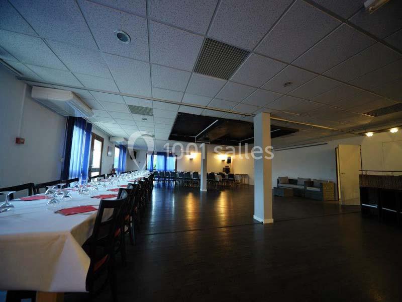 Salle spacieuse avec tables dressées pour un repas, chaises alignées et éclairage tamisé.