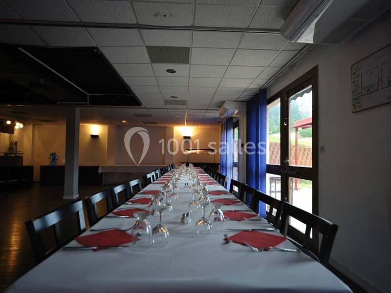 Table dressée avec une nappe blanche, verres retournés et serviettes rouges, dans une salle lumineuse avec baies vitrées.