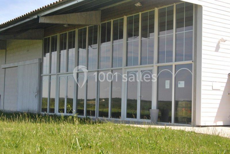 Façade vitrée d’un bâtiment avec des arches, entourée de verdure et reflétant le paysage environnant.