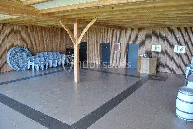 Salle vide avec sol carrelé, murs en bois, plafond à poutres apparentes, chaises empilées et comptoir en bois.