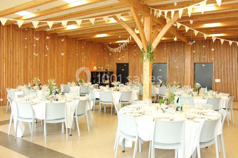 Salle de réception décorée avec des tables rondes dressées, guirlandes suspendues et murs en bois.