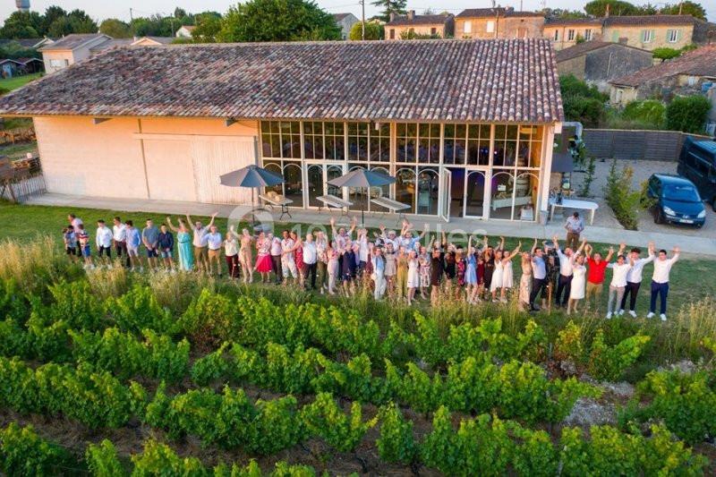 Un groupe de personnes rassemblées devant un bâtiment moderne entouré de vignes, vu en plongée.