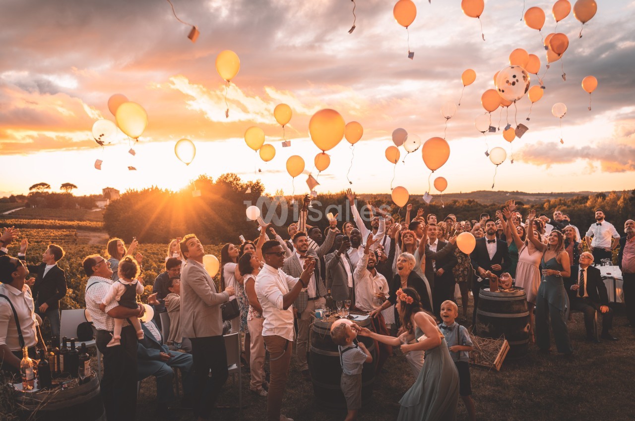 Groupe de personnes libérant des ballons colorés dans un paysage champêtre au coucher du soleil.