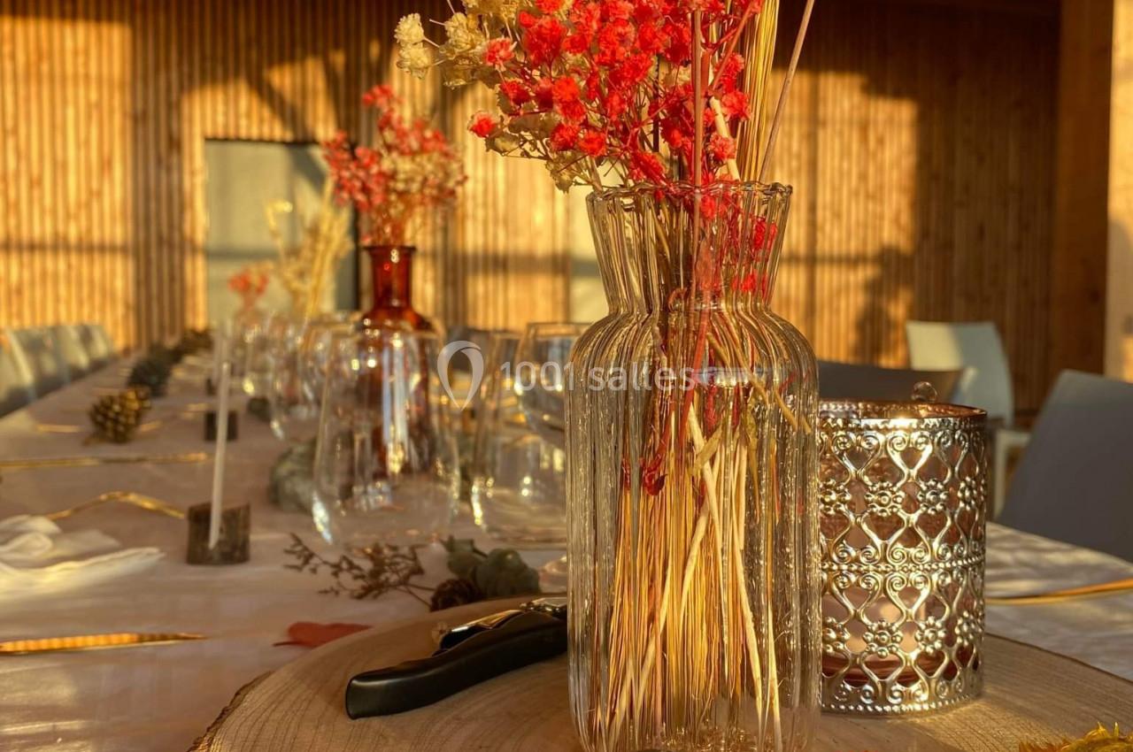 Centre de table automnal avec fleurs séchées dans un vase en verre, bougie décorative et rondin de bois.