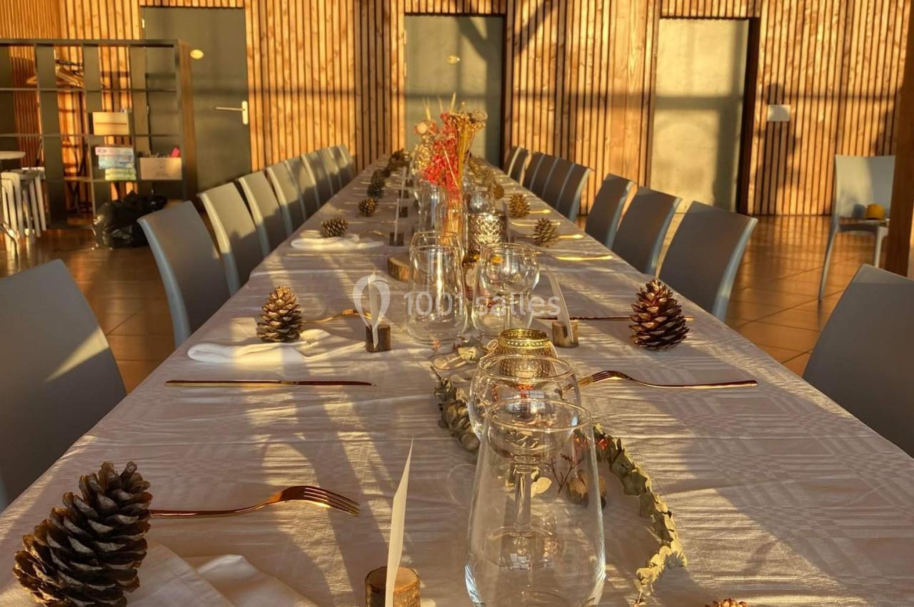 Table décorée pour un repas, ornée de pommes de pin, bougies et éléments naturels, dans une salle en bois éclairée par le…
